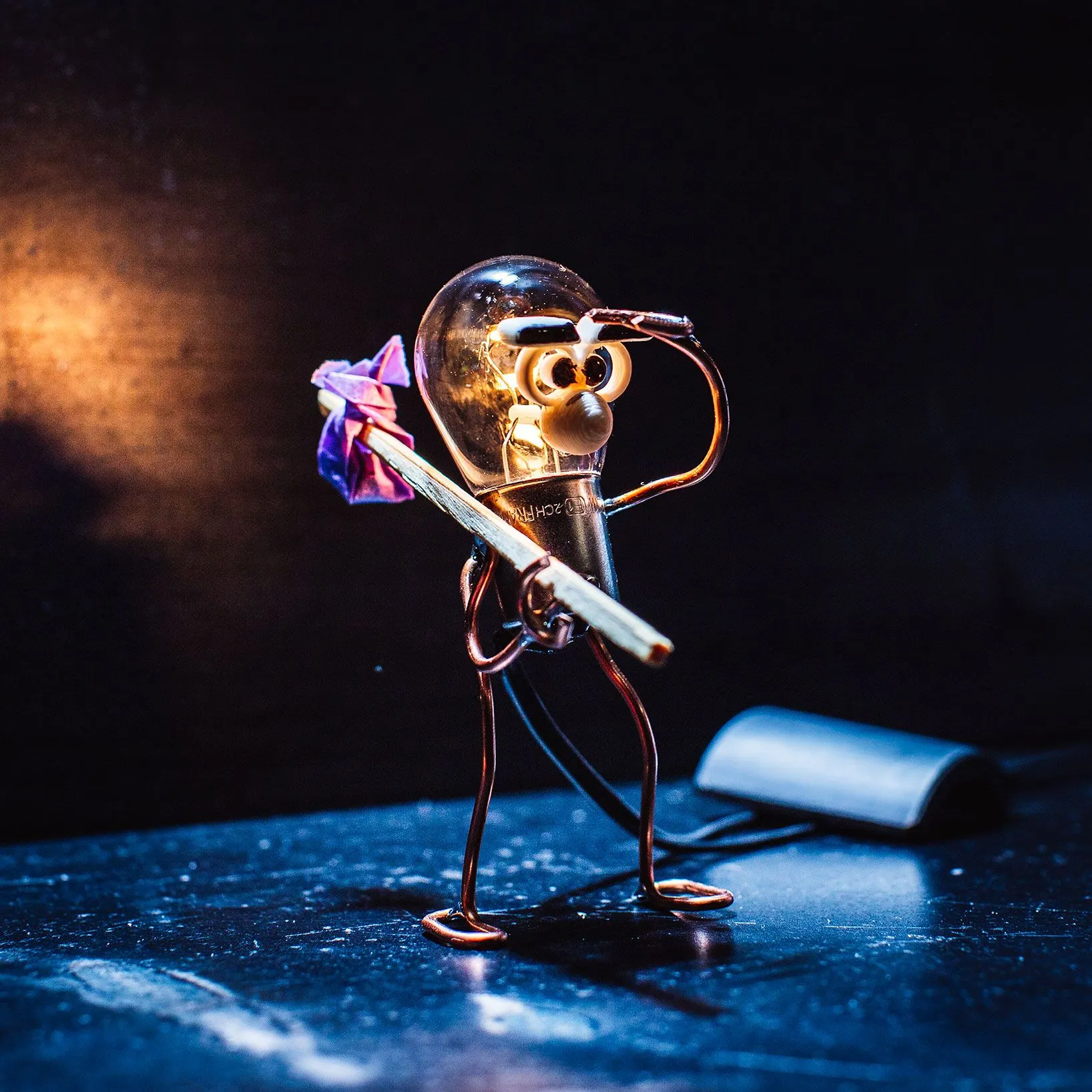 A small wire-and-lightbulb figure holding a pipe, standing on a dark blue surface