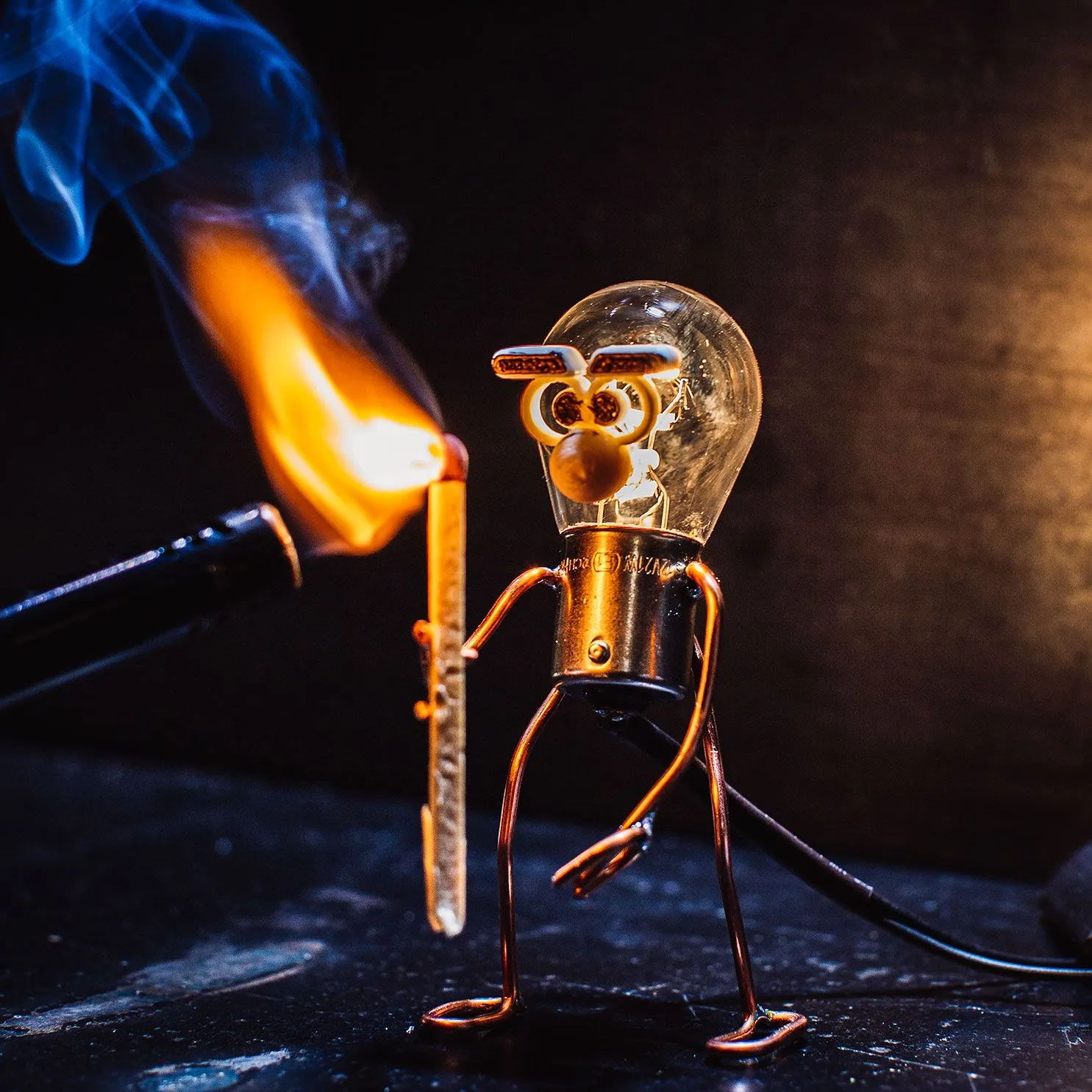 Lamp, a little wire figure with a lightbulb head, lighting a match